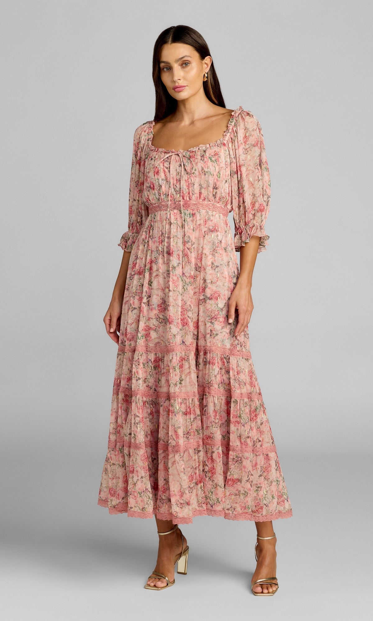 A woman stands against a plain gray background wearing the Mac Duggal 8330 tea-length party dress in Pink Multi, featuring puff sleeves and elegant detailing for a timeless and graceful look. She completes the outfit with ankle-strap heels.